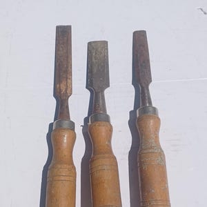 May include: Three wooden-handled chisels with metal blades. The chisels are all different sizes and have a worn, vintage look.