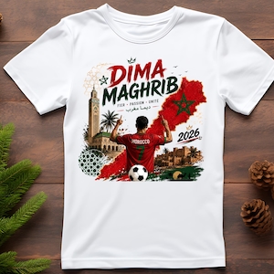 May include: A white t-shirt featuring a graphic print of a soccer player in a red jersey with the number 7, a soccer ball, the text DIMA MAGHRIB, FIER PASSION UNITE, 2026, a map of Morocco with a green star, a tall tower, palm trees, and a desert scene.