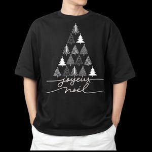 Peut inclure: T-shirt noir avec un motif d'arbre de Noël blanc composé de différentes illustrations d'arbres. Le texte en cursive "Joyeux Noël" est en dessous. Le t-shirt a une coupe ample et décontractée.