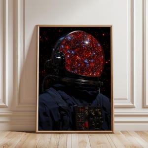 以下が含まれることがあります： 暗い宇宙服を着て反射バイザー付きのヘルメットを被った宇宙飛行士を描いた額装されたウォールアートプリント。バイザーには、黒い背景に赤と青の星が密集した鮮やかなフィールドが映し出されており、深宇宙の星雲を彷彿とさせるデザインとなっている。