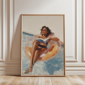 Puede incluir: Una lámina artística enmarcada que representa a una persona de pelo oscuro con gafas de sol y bañador oscuro, relajándose en un flotador naranja translúcido mientras lee un libro abierto en el agua azul con pinceladas visibles.