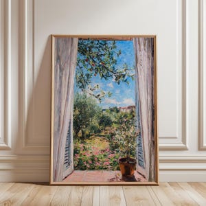 Op de afbeelding: Een ingelijst schilderij toont een levendige buitenscène door een open raam. Het kunstwerk toont een weelderige tuin met roze bloemen, olijfbomen en een heldere blauwe lucht. Een potplant staat op de vensterbank en witte gordijnen omlijsten het uitzicht.