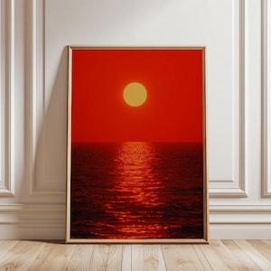 Può includere: Una stampa artistica rettangolare incorniciata che raffigura un vibrante tramonto rosso su un oceano scuro. Un sole circolare giallo solido è posizionato al centro superiore della composizione, proiettando un riflesso luminoso sull'acqua.