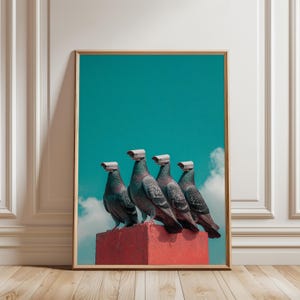 May include: Framed art print featuring five pigeons perched on a red structure, each with a surveillance camera attached to its head. The background is a vibrant teal sky with wisps of clouds. The artwork is displayed in a room with a wooden floor.