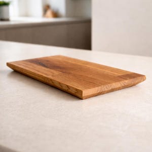 Pu&ograve; includere: Un tagliere rettangolare in legno con finitura a venatura naturale. La tavola ha un bordo smussato su un lato ed &egrave; realizzata in legno marrone chiaro. Il tagliere &egrave; esposto su una superficie di colore chiaro.