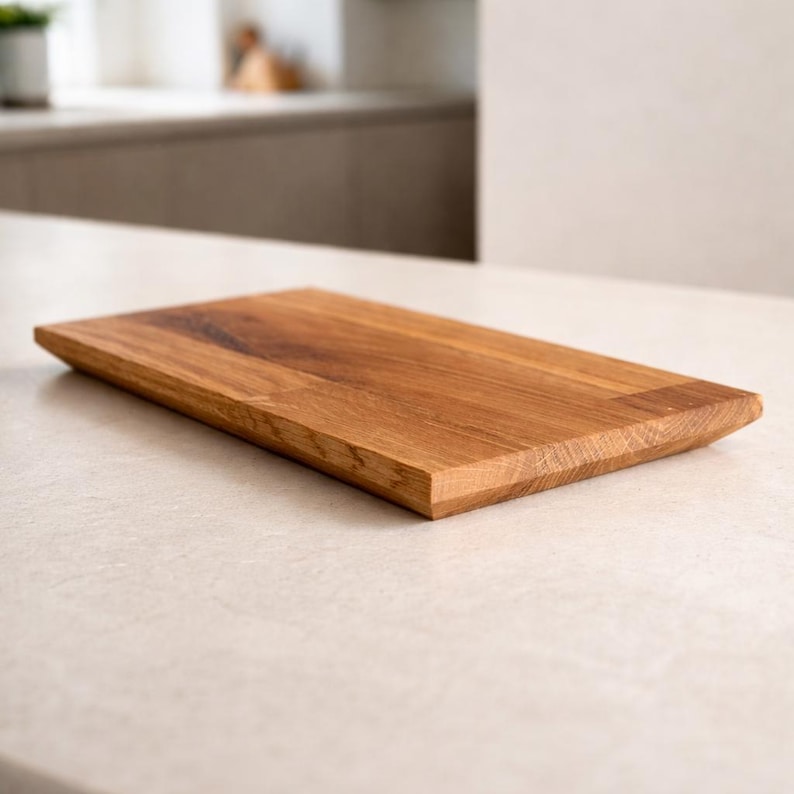 Pu&ograve; includere: Un tagliere rettangolare in legno con finitura a venatura naturale. La tavola ha un bordo smussato su un lato ed &egrave; realizzata in legno marrone chiaro. Il tagliere &egrave; esposto su una superficie di colore chiaro.