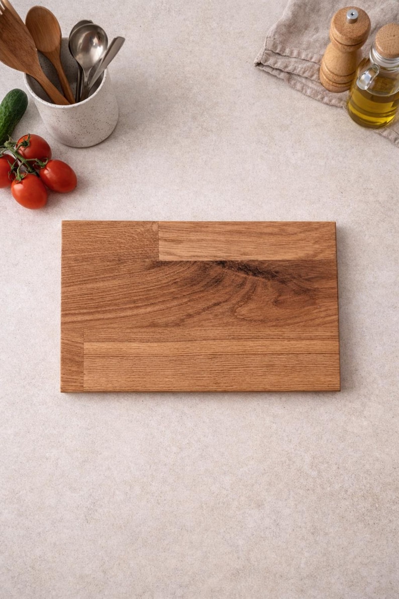 Pu&ograve; includere: Un tagliere rettangolare in legno con un motivo a venature naturali. La tavola &egrave; circondata da utensili da cucina, pomodori, un cetriolo, olio d'oliva e saliere e pepiere. La tavola misura circa 30 cm di lunghezza e 20 cm di larghezza.