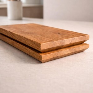 Pu&ograve; includere: Due taglieri rettangolari in legno impilati l'uno sull'altro. I taglieri sono in legno marrone chiaro con venature visibili e un bordo smussato. I taglieri sono su una superficie di colore chiaro.