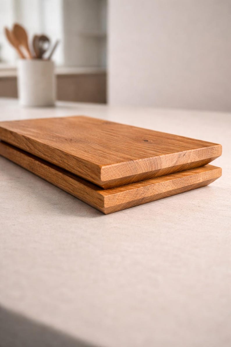 Pu&ograve; includere: Due taglieri rettangolari in legno impilati l'uno sull'altro. I taglieri sono in legno marrone chiaro con venature visibili e un bordo smussato. I taglieri sono su una superficie di colore chiaro.