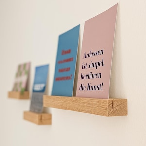 Op de afbeelding: Houten planken aan een witte muur, elk met een kaart. De kaarten zijn in verschillende kleuren, waaronder blauw en roze, met donkere tekst. De planken zijn gemaakt van lichtgekleurd hout.