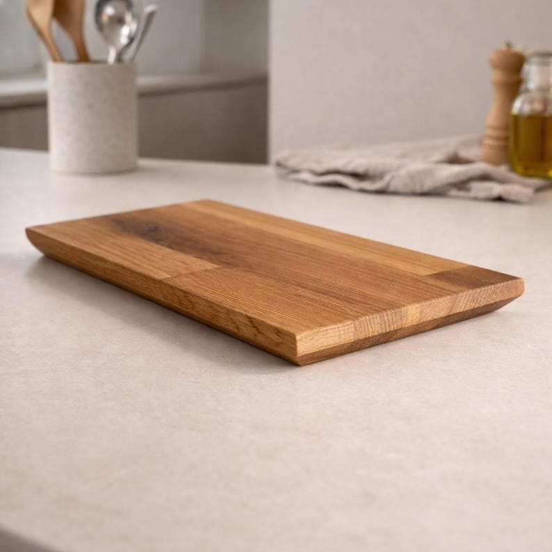 Pu&ograve; includere: Un tagliere rettangolare in legno con finitura a venature naturali. La tavola &egrave; in legno marrone chiaro e ha un bordo smussato su un lato. &Egrave; un oggetto da cucina, probabilmente utilizzato per la preparazione del cibo.