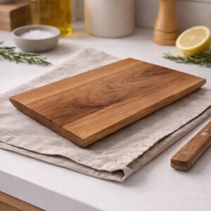Pu&ograve; includere: Un tagliere rettangolare in legno con finitura marrone chiaro poggia su un panno di lino beige. La tavola &egrave; circondata da oggetti da cucina, tra cui una ciotola di sale, una bottiglia d'olio e un limone.