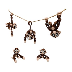May include: Five brown monkey figurines with white accents. Two monkeys hang from a rope, one hangs from a hook, and two sit on a white surface. The monkeys have large, round eyes and articulated limbs.
