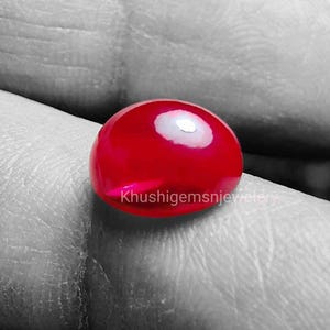 Może przedstawiać: Czerwony, błyszczący kamień szlachetny w szlifie kaboszonowym, o gładkiej, wypolerowanej powierzchni. Kamień jest okrągły i ma lekko wypukły kształt.