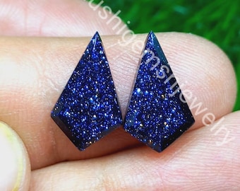 May include: Two kite-shaped blue sandstone cabochons featuring a deep navy blue base with sparkling metallic flecks throughout. The stones have a flat surface and angled edges. The text Khushigemsjewelry is visible across the stones.