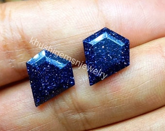 May include: Two kite-shaped blue sandstone gemstones with a sparkling, glittery finish. The dark blue surface features numerous reflective flecks. The text khushigemsnjewelry is overlaid across the center of the two faceted stones.