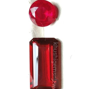 Puede incluir: Dos piedras preciosas rojas sobre una superficie blanca. Una es redonda, la otra rectangular con el texto "Khushigemsnjewelry" en el lateral. Las gemas son de un color rojo intenso y rico.