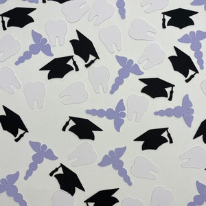 May include: A collection of confetti featuring graduation caps, teeth, and caduceus symbols. The confetti is black, white, and purple.