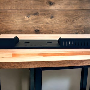 May include: Black metal rack with slots and holes, designed for organizing and storing items. The rack is sitting on a wooden table.