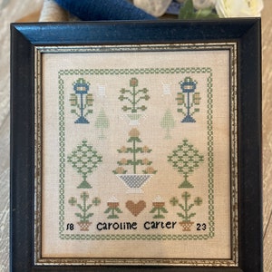 May include: A framed cross-stitch embroidery with a floral design in shades of green, blue, and brown. The embroidery includes a heart and the text "Caroline Carter 23".