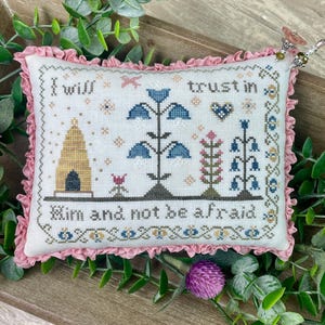 May include: A white pillow with pink ruffles around the edges. The pillow is embroidered with a beehive, flowers, and the text "I will trust in Him and not be afraid".