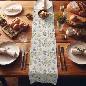 Op de afbeelding: Een lichtgekleurde tafelloper met Pasen als thema, met een herhaald patroon van lammetjes, kuikens en paaseieren. De loper ligt op een houten tafel met borden, bestek en etenswaren.