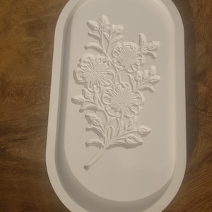 Könnte beinhalten: Weißes ovales Tablett mit einem erhabenen Blumendesign. Das Design zeigt drei Blumen und Blätter.