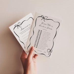 Pu&ograve; includere: Due biglietti bianchi con scritte nere e bordi decorativi. Un biglietto recita "Memories" e l'altro "Guess Who Bride or Groom". Il biglietto "Guess Who" ha un elenco di domande. I biglietti sono tenuti da una mano.