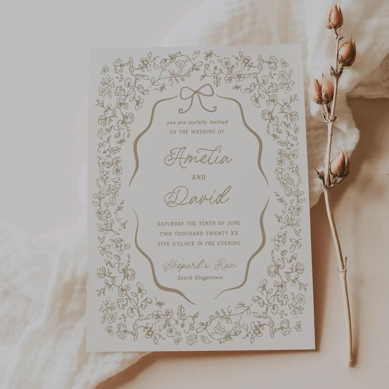 May include: A wedding invitation with a floral design in gold on a white background. The invitation includes the names "Amelia" and "David", along with the wedding date and time. The text is framed by a floral border.