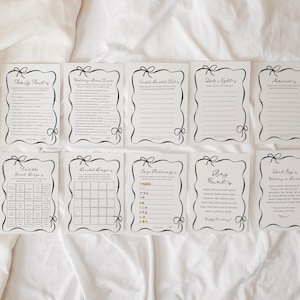 Pu&ograve; includere: Una collezione di carte bianche con testo nero e bordi decorativi. Ogni carta presenta un gioco o un'attivit&agrave; diversa, tra cui "Family Find", "Wedding Mime Game" e "Ring Hunt". Le carte sono disposte su una superficie bianca.