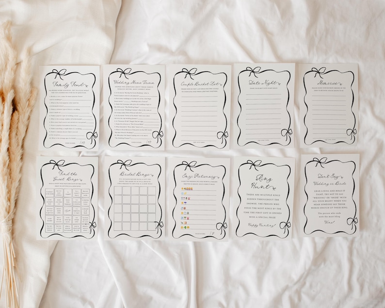 Pu&ograve; includere: Una collezione di carte bianche con testo nero e bordi decorativi. Ogni carta presenta un gioco o un'attivit&agrave; diversa, tra cui "Family Find", "Wedding Mime Game" e "Ring Hunt". Le carte sono disposte su una superficie bianca.