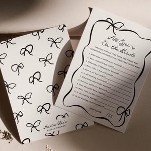 Pu&ograve; includere: Due biglietti bianchi per un gioco di addio al nubilato. Un biglietto presenta un motivo di fiocchi neri, con il testo "Amelia Rae's Bridal Shower". L'altro biglietto ha il testo "All Eyes On the Bride" e un elenco di domande.