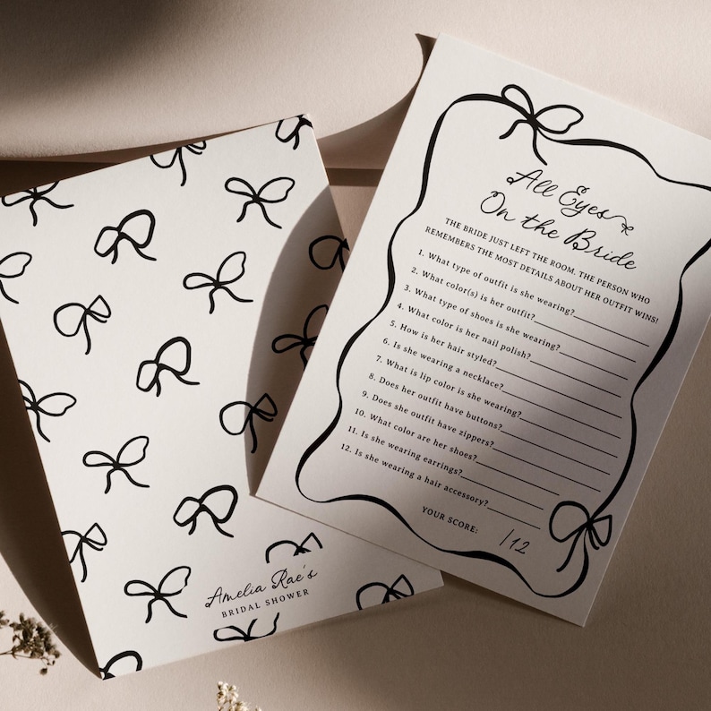 Pu&ograve; includere: Due biglietti bianchi per un gioco di addio al nubilato. Un biglietto presenta un motivo di fiocchi neri, con il testo "Amelia Rae's Bridal Shower". L'altro biglietto ha il testo "All Eyes On the Bride" e un elenco di domande.