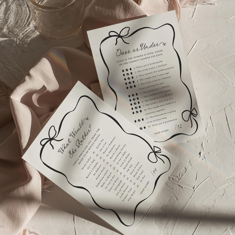 Pu&ograve; includere: Due fogli di carta bianchi con testo nero e un bordo decorativo a fiocco. Un foglio recita "What Would She Rather?" con un elenco di opzioni. L'altro recita "Over or Under?" con una serie di domande. Un bicchiere &egrave; sullo sfondo.