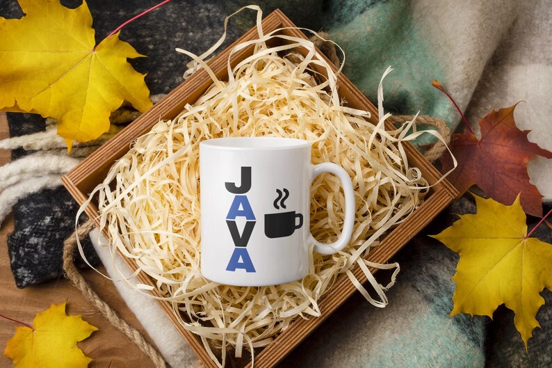 Pu&ograve; includere: Tazza in ceramica bianca con la scritta "JAVA" in lettere nere e blu e una grafica di tazza di caff&egrave; nera. La tazza &egrave; in una scatola di legno piena di paglia, con foglie autunnali sullo sfondo.