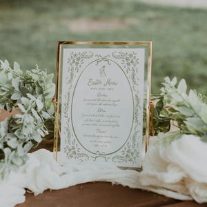 Pu&ograve; includere: Un menu incorniciato in oro con sfondo bianco e illustrazioni floreali verdi. Il menu &egrave; per una celebrazione pasquale e indica la data 20 aprile 20XX. Il menu comprende antipasti, piatto principale, dessert e caff&egrave; e t&egrave;.