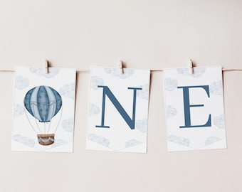 May include: A three-piece banner set featuring white rectangular cards with light blue cloud patterns. The first card displays a blue hot air balloon, while the second and third cards feature the dark blue capital letters N and E.