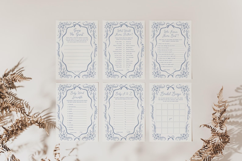 Pu&ograve; includere: Sei biglietti per giochi di baby shower con bordi floreali blu e testo. Le carte includono giochi come "Indovina l'ospite" e "Bingo nuziale". Le carte sono disposte su una superficie bianca con piante secche in primo piano.
