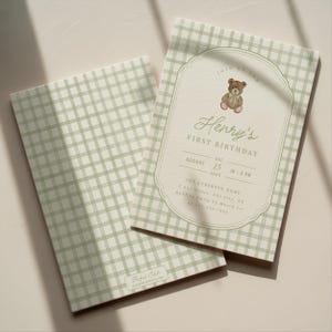 May include: Two baby shower invitations. The invitations have a light green gingham pattern. One invitation has a decorative border with a teddy bear illustration and the text "Henry's First Birthday".