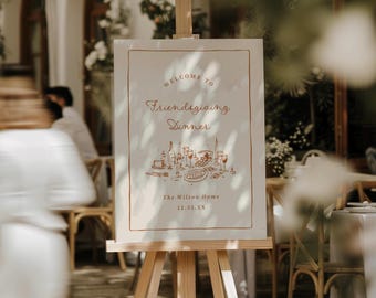 May include: A rectangular white welcome sign on a wooden easel featuring copper-colored text that reads Welcome to Friendsgiving Dinner, The Wilson Home, 11.25.XX, and a line drawing of a dinner table setting with plates and glasses.