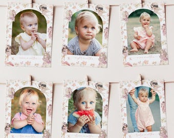 May include: Six rectangular photo cards hanging on a string, each featuring a portrait of a baby framed by an arched border with fairy and floral illustrations. The cards are labeled with text indicating months of age, including seven, eight, nine, ten, eleven, and twelve months, with soft pink and beige tones.