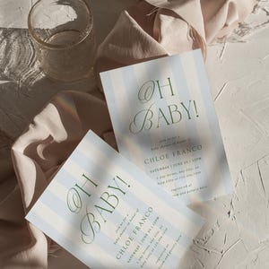 May include: Two baby shower invitations with blue and white stripes and the text "OH BABY!" in green script. The invitations include details for Chloe Franco's baby shower. A clear glass and draped fabric are also in the image.