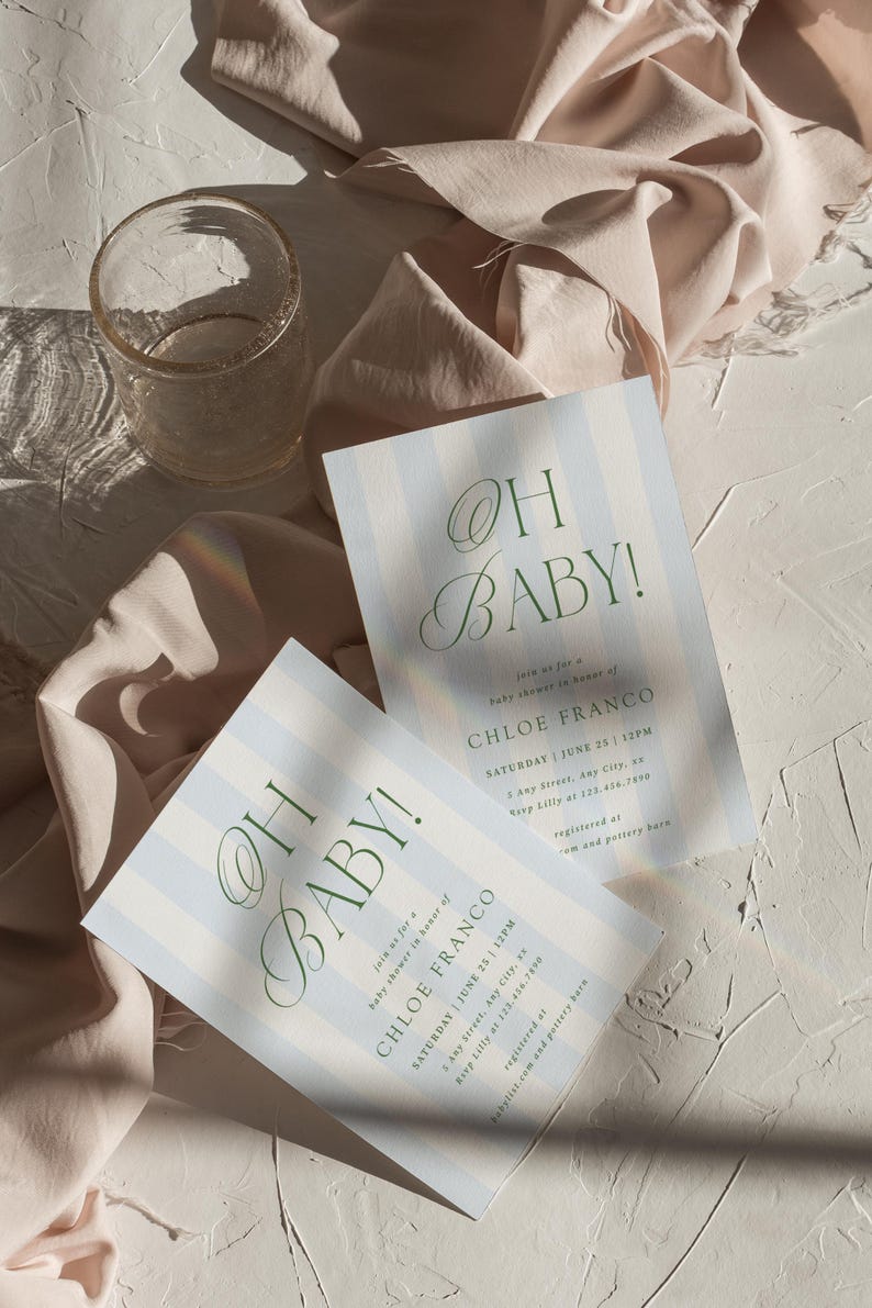 May include: Two baby shower invitations with blue and white stripes and the text "OH BABY!" in green script. The invitations include details for Chloe Franco's baby shower. A clear glass and draped fabric are also in the image.
