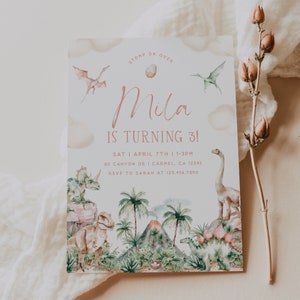 May include: A dinosaur-themed birthday party invitation with a pink and white color scheme. The invitation features a watercolor illustration of dinosaurs, a volcano, and palm trees. The text on the invitation reads "STOMP ON OVER Mila IS TURNING 3! SAT | APRIL 7TH | 1-3PM 82 CANYON DR | CARMEL, CA 12345 RSVP TO SARAH AT 123.456.7890"