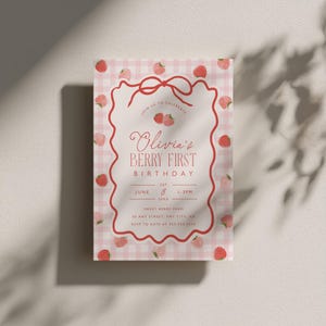 May include: A pink and white gingham patterned invitation with a red scalloped border. The invitation reads "Olivia's Berry First Birthday" with strawberry illustrations. The text includes the date, time, and location.