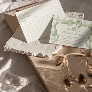 Pode incluir: Dois cart&otilde;es de receitas com texto, "Receita" e "Compartilhe uma Receita", repousam sobre uma superf&iacute;cie de madeira clara. Os cart&otilde;es t&ecirc;m um design minimalista com detalhes verdes. O fundo &eacute; um tecido neutro, e plantas secas est&atilde;o em primeiro plano.