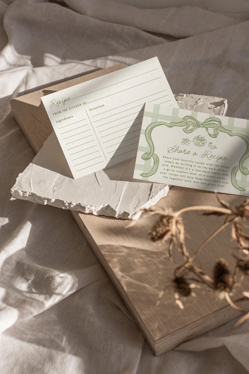 Pode incluir: Dois cart&otilde;es de receitas com texto, "Receita" e "Compartilhe uma Receita", repousam sobre uma superf&iacute;cie de madeira clara. Os cart&otilde;es t&ecirc;m um design minimalista com detalhes verdes. O fundo &eacute; um tecido neutro, e plantas secas est&atilde;o em primeiro plano.