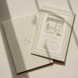 Peut inclure: Deux cartes rectangulaires avec un motif à rayures verticales beige et blanc. L'une présente un dessin au trait d'une devanture de café, un landau et le texte A BABY IS BREWING! Chloe Rhodes, Saturday June 25, 12PM. L'autre montre une tasse de café, un croissant et une cafetière.