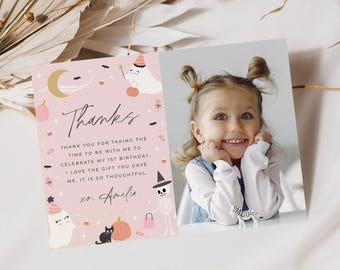 Può includere: Un biglietto di ringraziamento rettangolare con sfondo rosa chiaro e illustrazioni a tema Halloween tra cui fantasmi, uno scheletro, un gatto nero, zucche e una luna crescente. Il testo recita: Thanks, Thank you for taking the time to be with me to celebrate my 1st birthday, I love the gift you gave me, it is so thoughtful, xo, Amelia. Una foto di un bambino piccolo con i capelli raccolti in due chignon è allegata sul lato destro.