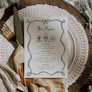 Puede incluir: Una tarjeta de menú impresa con un borde decorativo verde y texto. El menú incluye entrantes, guarniciones y postres. La tarjeta está sobre un plato blanco con un tenedor y un cuchillo dorados.